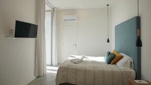 Moderni hotellihuone, jossa on sänky, taulutelevisio, ilmastointilaite ja näkymä ulos.