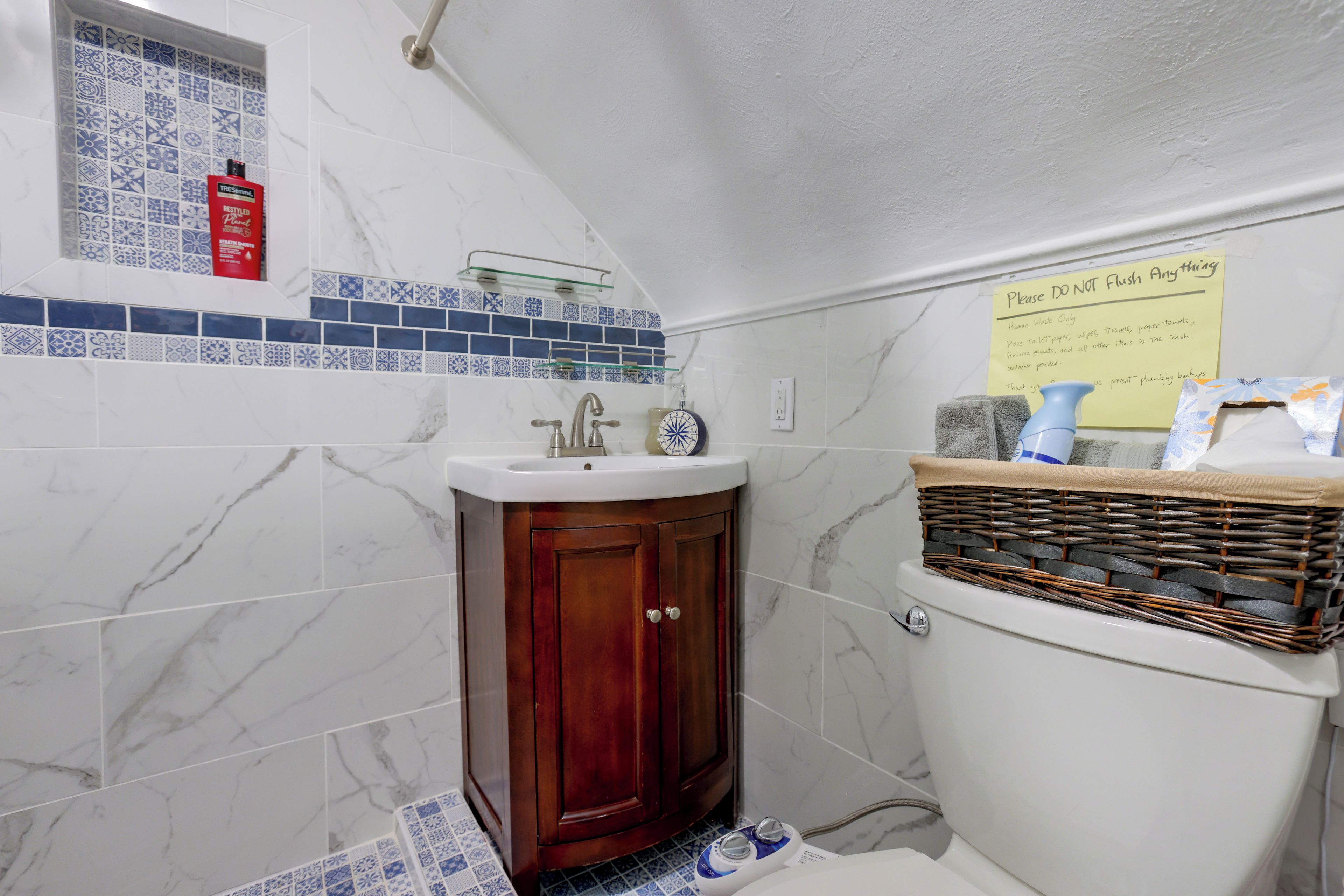Une salle de bain avec un lavabo blanc, un meuble en bois et des toilettes, avec un panier rempli de serviettes à proximité.