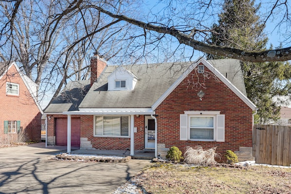 A two-story brick house with a red door, a small attached garage, and a covered porch.