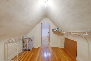 A narrow attic space with a sloped ceiling, wooden flooring, and a white door leading to another room.