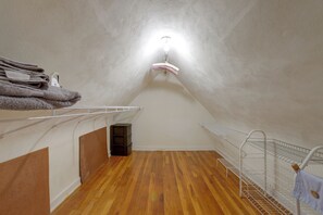 Un petit dormitori a l'àtic amb sostre inclinat, terres de fusta, paret blanca i llum penjant.