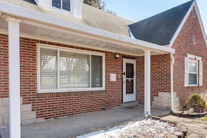 A red brick house with a covered porch, a front door, and a small garden area.