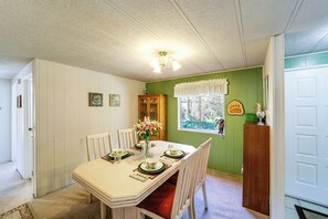 A dining room with a table set for four, a vase with flowers, and a window with a view of greenery. - Cozy Waterfront Home w/ Mtn View Near Leavenworth (Peshastin)