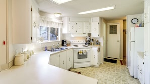 A compact kitchen with white cabinets, a stove, a sink, and a refrigerator. - Cozy Waterfront Home w/ Mtn View Near Leavenworth (Peshastin)