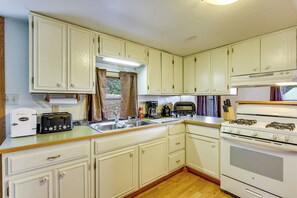 A compact kitchen with white cabinets, a gas stove, a toaster, and a sink.
