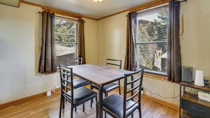 A dining area with a wooden table and chairs, a ceiling light, and a view of trees through the windows. - Steps to Lake Isabel & Trails! Mtn-View Hideaway (Rye)