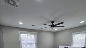 Un dormitorio con cama, ventilador de techo, ventana y escritorio.