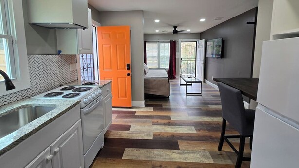 Una cocina compacta con estufa, lavamanos y una puerta naranja brillante que da a un dormitorio.