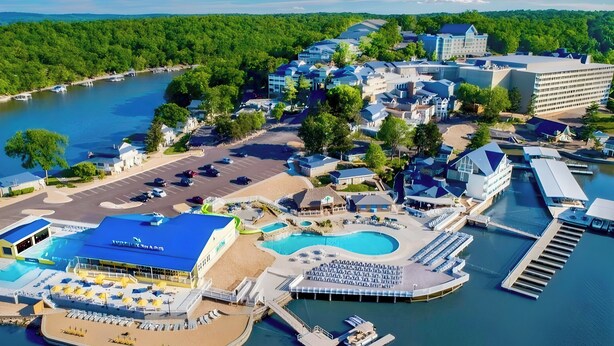 Vista aérea de un resort con un puerto deportivo, piscinas y un edificio grande de techo azul.