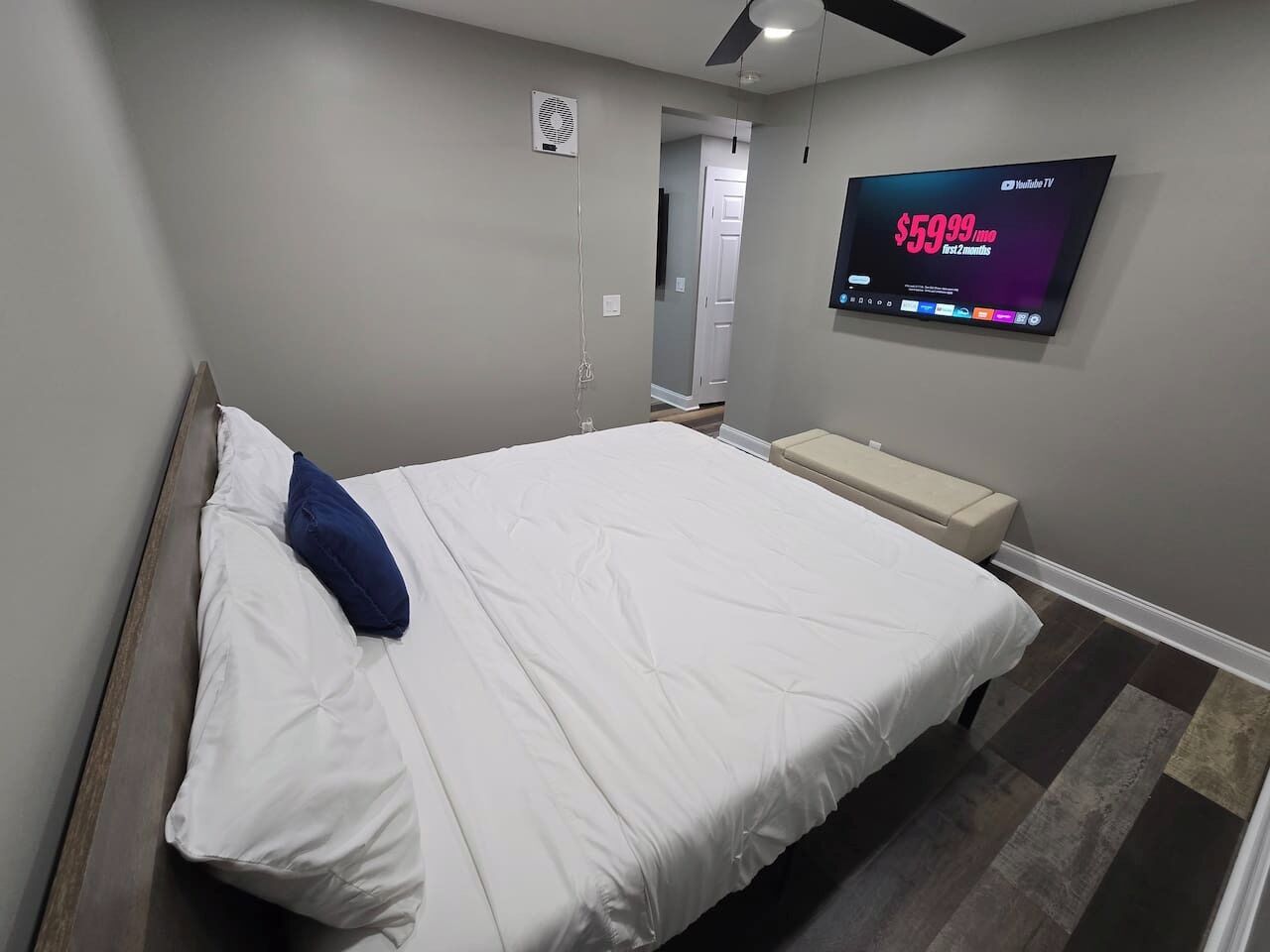A modern hotel room with a bed, a TV mounted on the wall, and a ceiling fan.