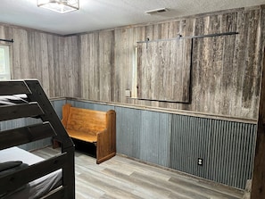 Una habitación con un banco de madera, una cama con cabecera, un panel de pared de madera y una ventana con marco de metal.