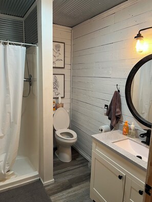 Un baño con ducha, inodoro, tocador y espejo.