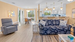 A spacious living room with a blue patterned sofa, a striped armchair, and a dining area with a table and chairs. - Coming soon brand new condos on the West end of Sanibel! Deeded beach access! (Sanibel)