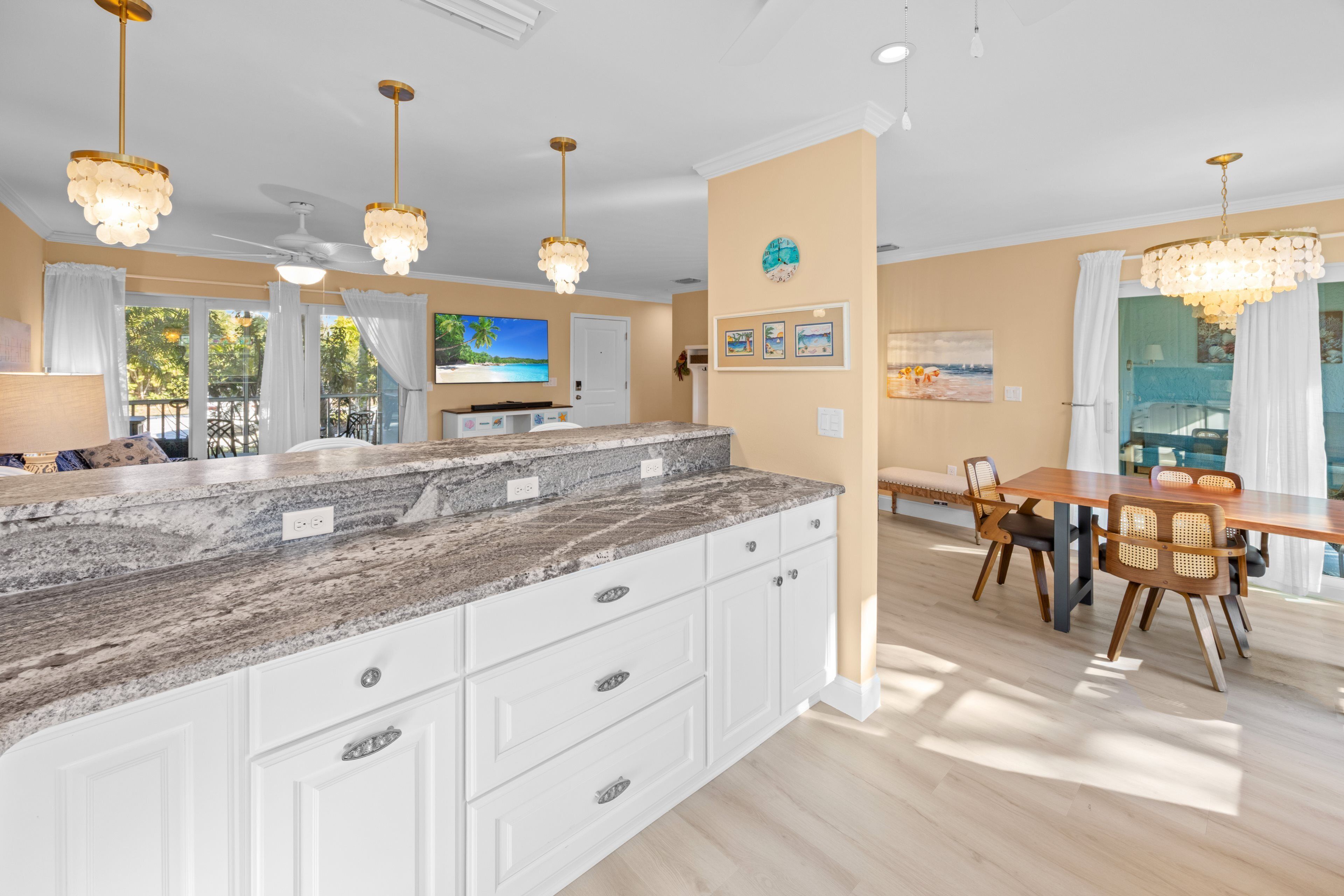 A spacious kitchen with a granite countertop, white cabinetry, and pendant lighting.