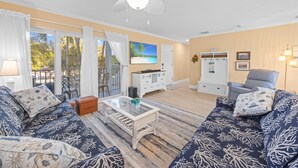 A living room with a sofa set, a coffee table, a TV, and a ceiling fan. - Coming soon brand new condos on the West end of Sanibel! Deeded beach access! (Sanibel)