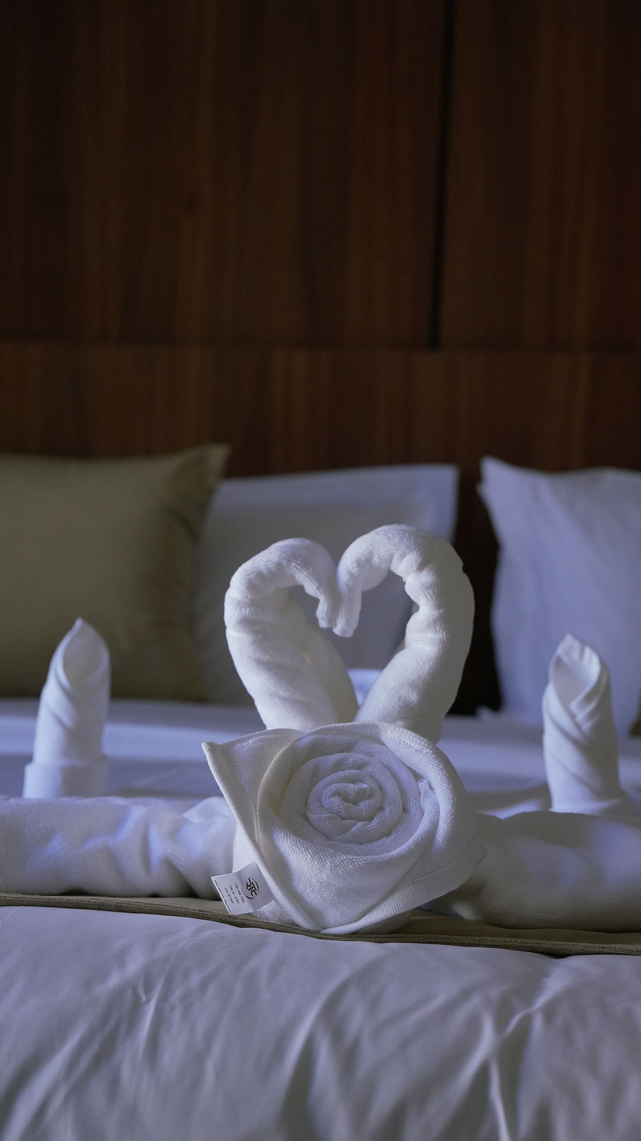 A bed with white linens and a towel arranged in a heart shape.