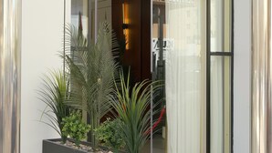 Una entrada de edificio moderna con puerta de vidrio, detector de incendios rojo y maceta con plantas.