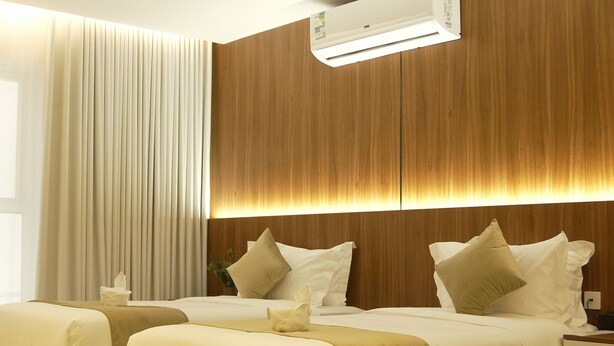 Una habitación de hotel moderna con una cama grande, una mesita de noche y un equipo de aire acondicionado incorporado.