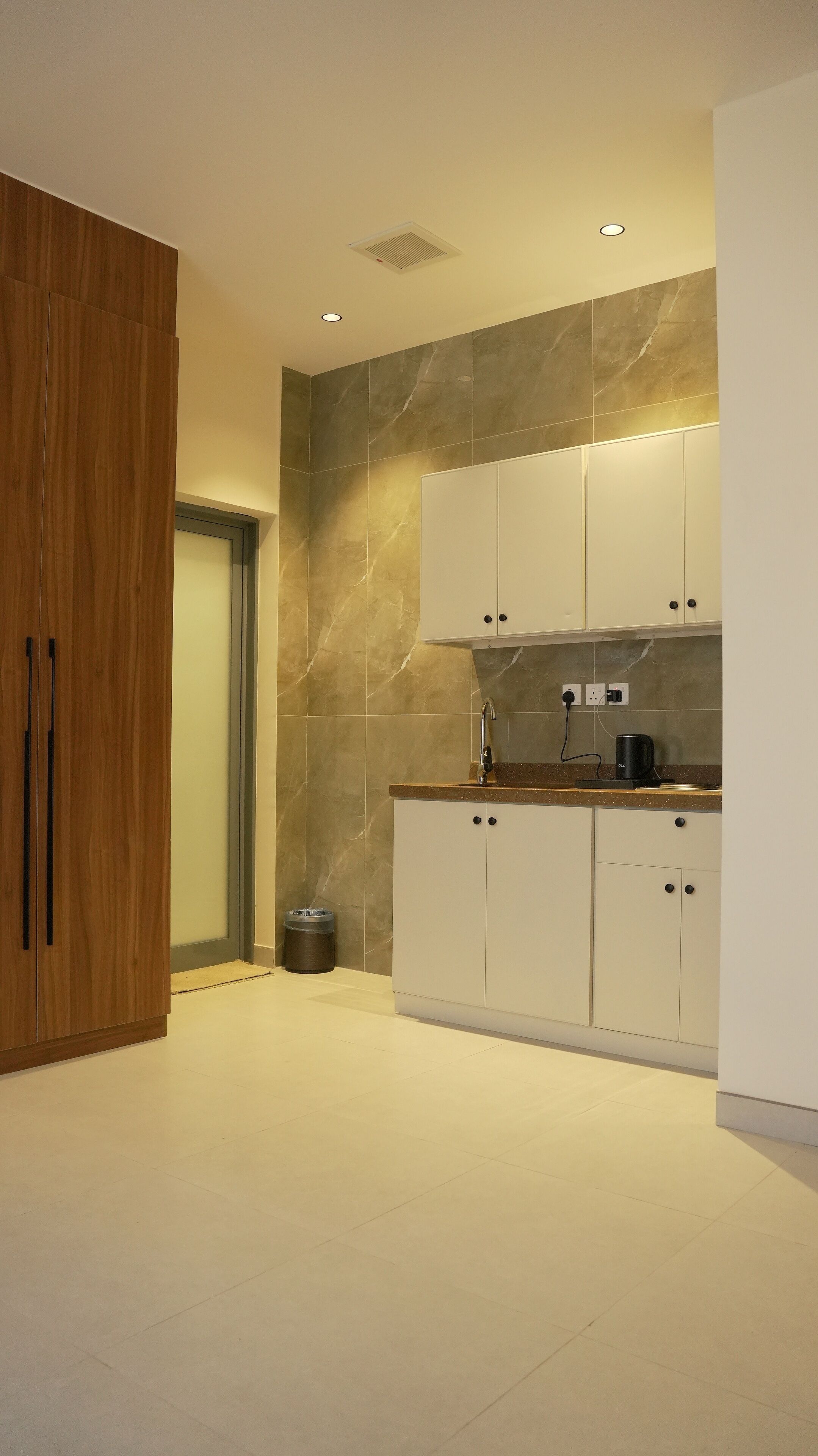 A modern kitchen with white cabinets, a marble backsplash, and a wooden door.