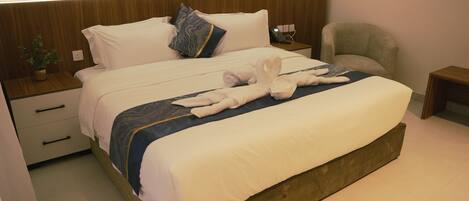 A hotel room with a large bed, a bedside table with a lamp, a chair, and a small table with a phone.
