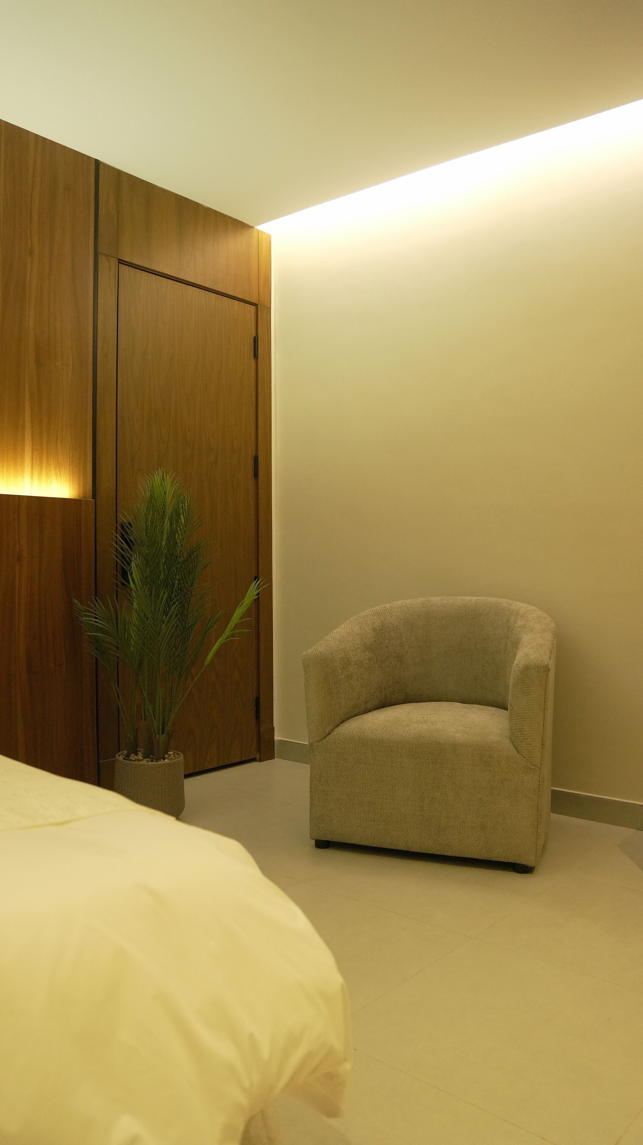 Um quarto com uma cama, uma cadeira, um vaso de planta e um guarda-roupa.