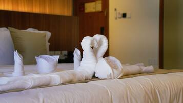 A neatly made bed with a folded towel arrangement in the shape of swans, a wooden headboard, and a beige pillow.