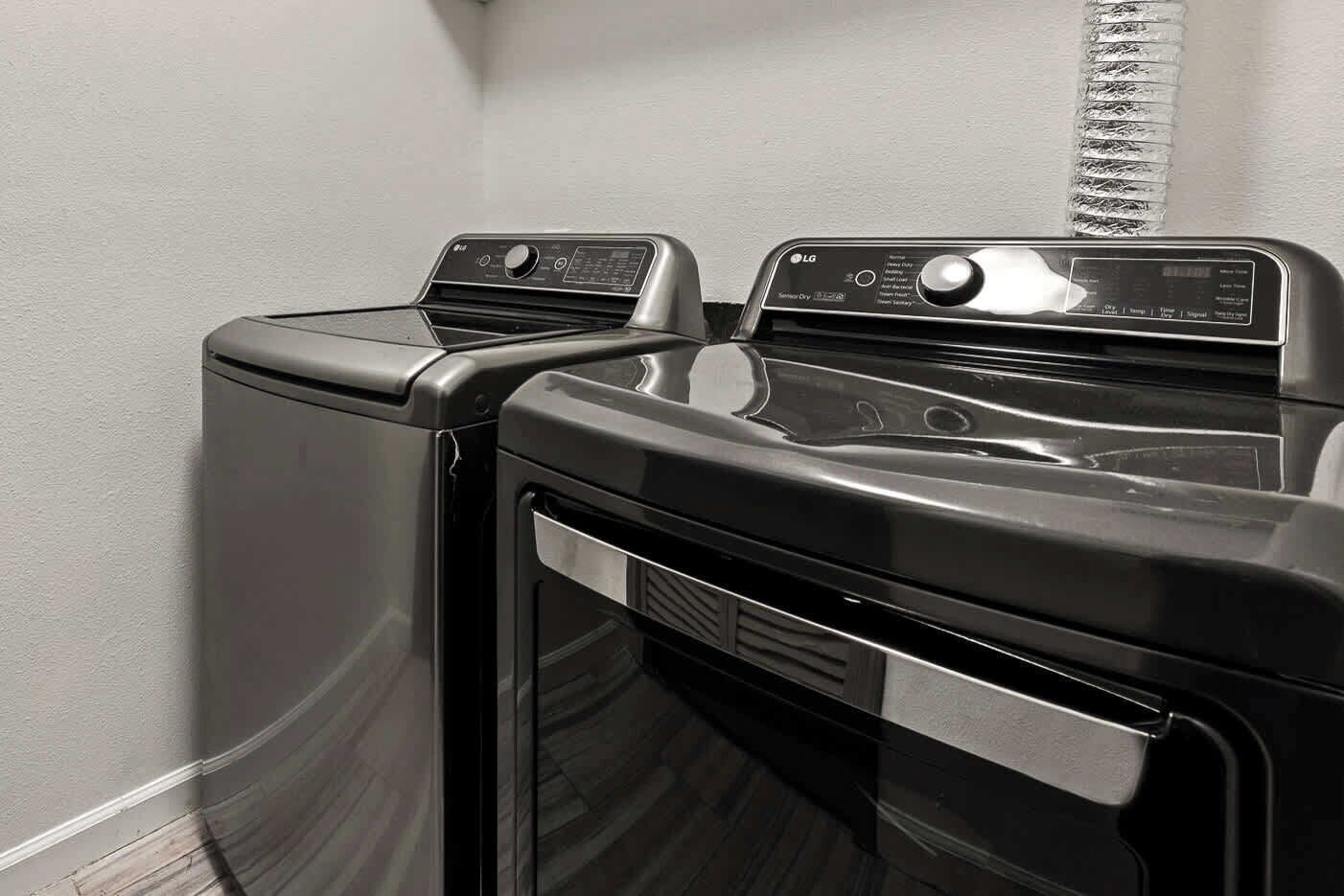 Une buanderie équipée de deux machines à laver et deux sèche-linge superposés, d’un panneau de commande et d’une bouche d’aération.