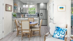 A modern kitchen with grey cabinets, a stainless steel refrigerator, and a dining area with wooden chairs and a table. - Seashells Unit 33 – Relaxing Sanibel Island Beach Retreat (Sanibel)