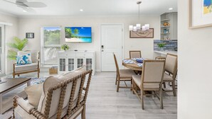 A modern living room with a sofa, a dining table with chairs, a TV, and a ceiling fan. - Seashells Unit 33 – Relaxing Sanibel Island Beach Retreat (Sanibel)