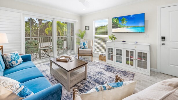 A spacious living room with a blue sofa, a wooden coffee table, and a TV mounted on the wall. - Seashells Unit 33 – Relaxing Sanibel Island Beach Retreat (Sanibel)