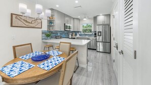 A modern kitchen with a central island, stainless steel appliances, and a dining area with a wooden table and chairs. - Seashells Unit 33 – Relaxing Sanibel Island Beach Retreat (Sanibel)