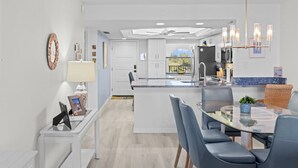 Een moderne keuken met witte kasten, een centraal eiland en een eetgedeelte met een glazen tafel en blauwe stoelen.
