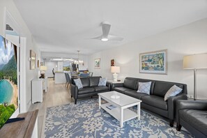Een moderne woonkamer met een witte salontafel, twee zwarte leren banken, een kamerkleed met patroon en een plafondventilator.