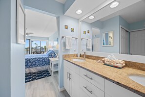 A modern bathroom with a large mirror, two sinks, and a bed with a blue and white patterned bedspread. - Lagoon & Gulf Views, Steps to the Beach, Beautifully Updated Condo (Sanibel)