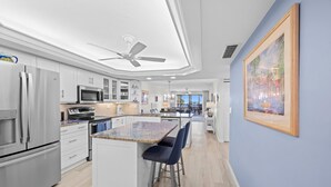 Een moderne keuken met witte kastjes, roestvrijstalen apparatuur en een centraal kookeiland met barstoelen.