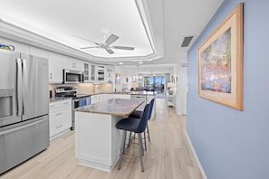 A modern kitchen with white cabinets, stainless steel appliances, and a central island with bar stools. - Lagoon & Gulf Views, Steps to the Beach, Beautifully Updated Condo (Sanibel)