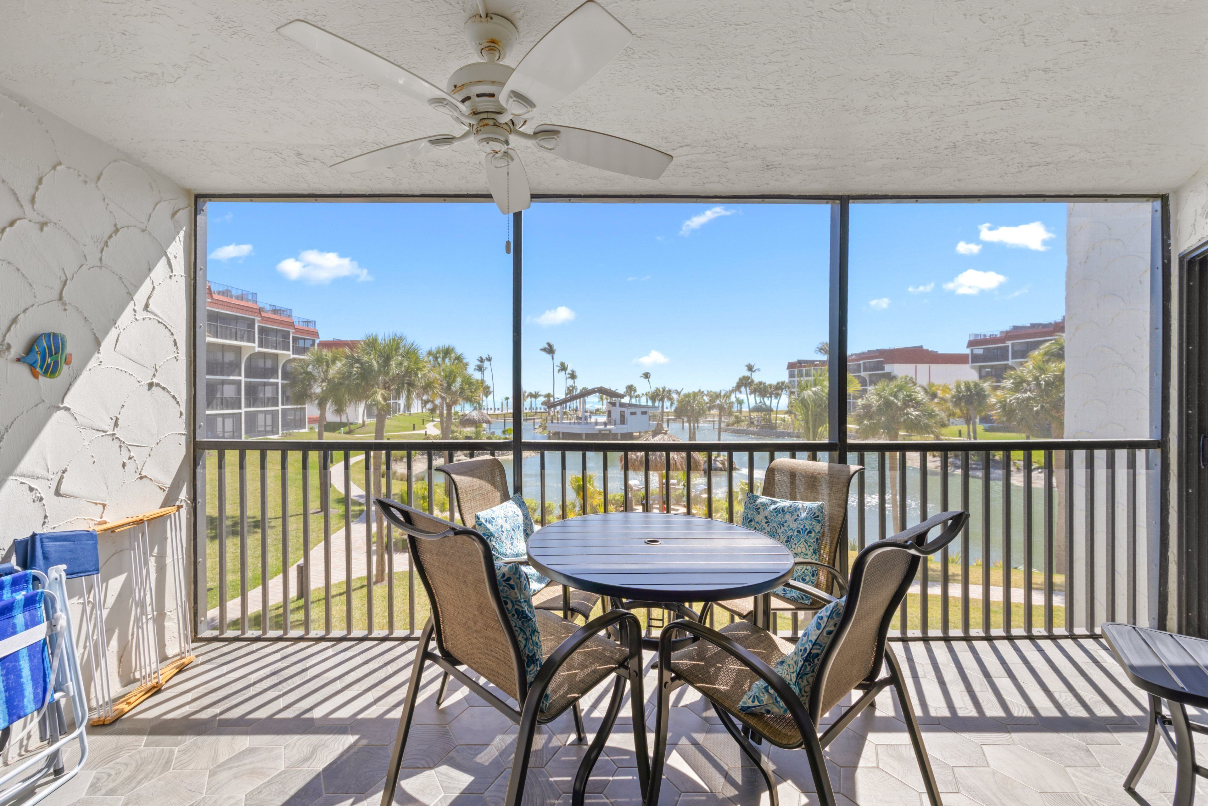A balcony with a table and chairs, a ceiling fan, and a view of buildings and palm trees.