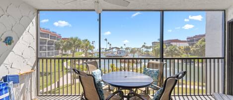 A balcony with a table and chairs, a ceiling fan, and a view of buildings and palm trees.