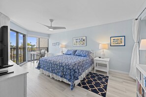 Een slaapkamer met een groot bed, een bureau, een stoel, een balkon met uitzicht en een plafondventilator.