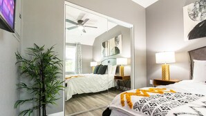 Een moderne hotelkamer met een bed, nachtkastjes, een spiegel, een plafondventilator en een potplant.