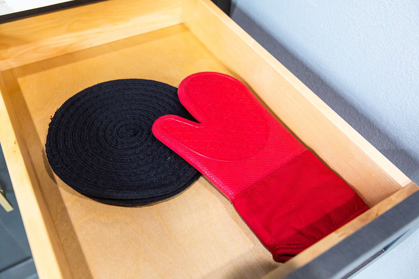 A wooden drawer containing a black circular object and a red oven mitt.