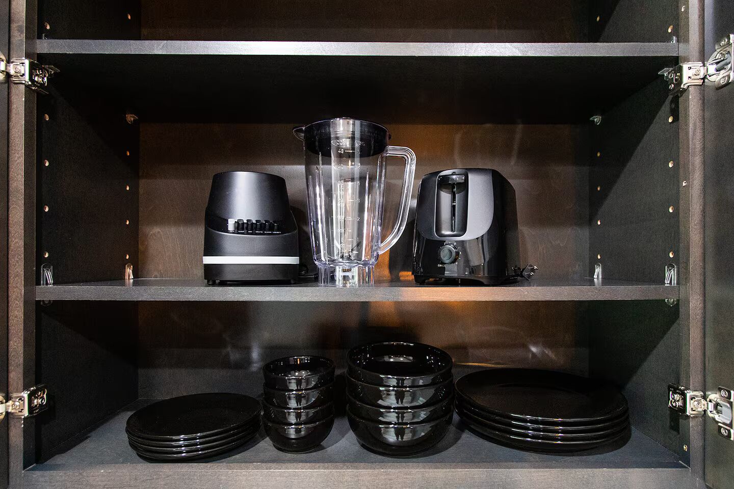 A kitchen shelf with a blender, a toaster, and stacked plates.