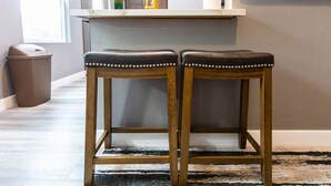 Twee houten barkrukken met metalen studs, een prullenbak, een potplant en een keukentrapje op de achtergrond.