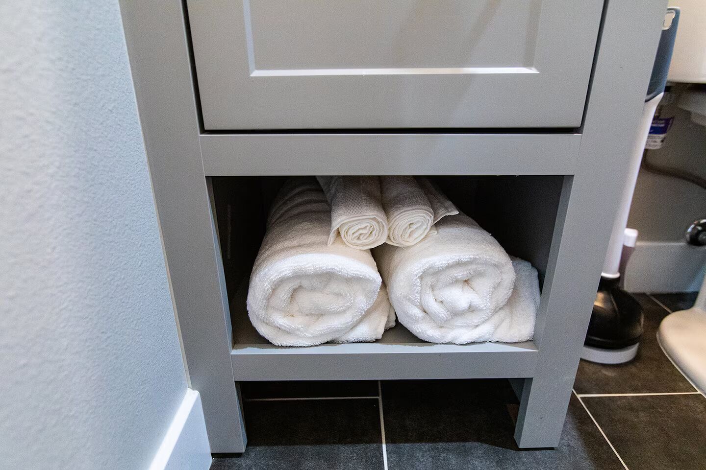 A bathroom with a grey cabinet containing rolled white towels.