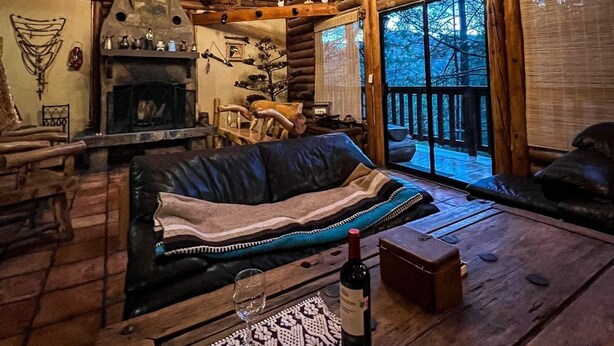 L’intérieur chaleureux d’un chalet, avec une cheminée, des meubles en bois et de grandes fenêtres donnant sur le paysage extérieur.