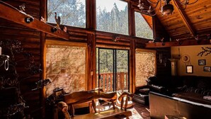 L’intérieur d’un chalet rustique, avec des murs en bois, de grandes fenêtres, un coin repas et un lustre.