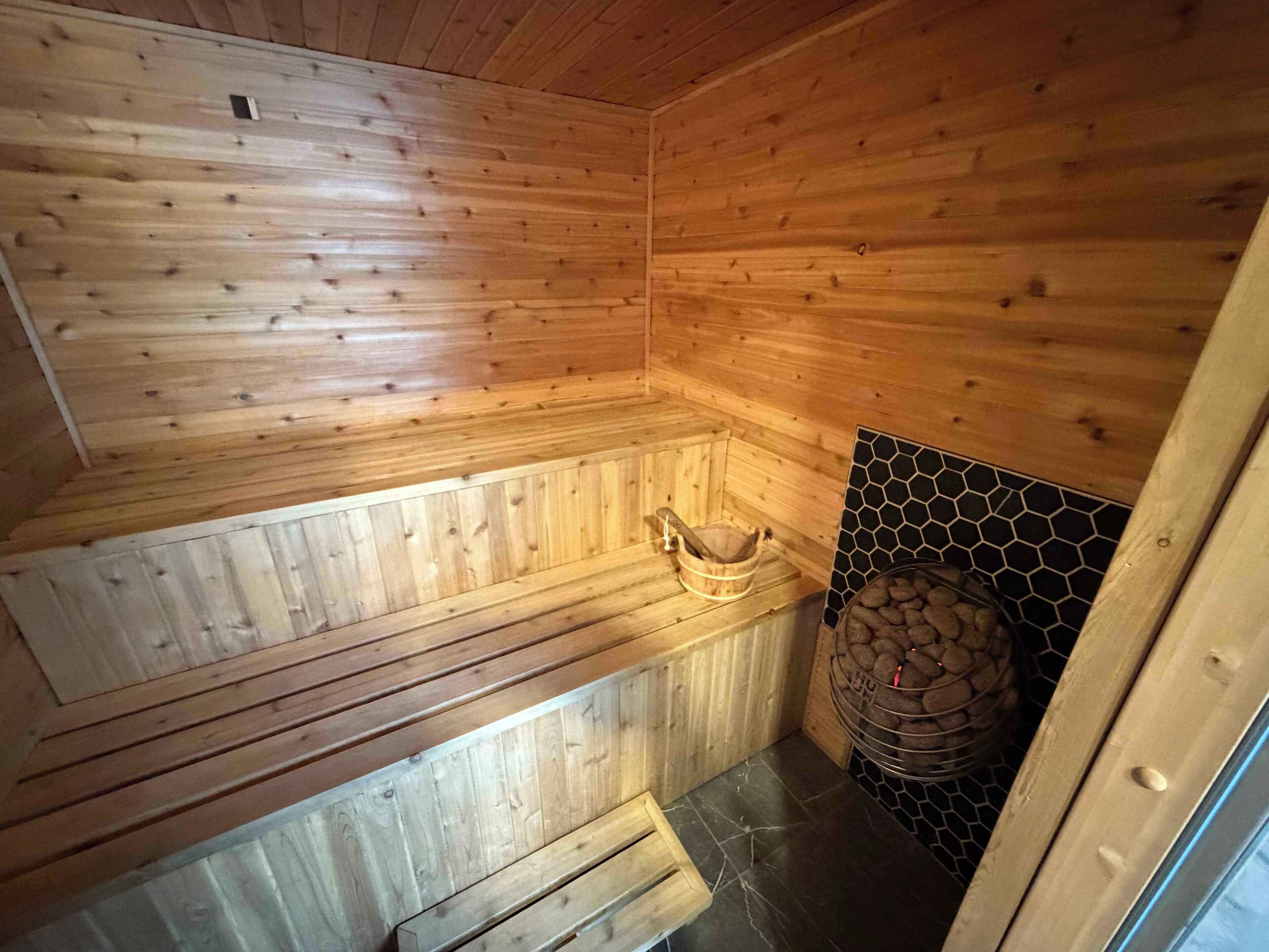 Puuinen sauna, jossa on penkki, puinen ämpäri ja kiviseinä.