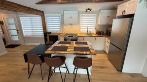 A modern kitchen with a central island, two chairs, and a refrigerator.