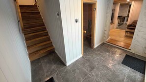 A staircase leading to a second floor, a glass door entrance, a living area with a sofa and coffee table, and a tiled floor.