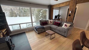 A modern living room with a sectional sofa, a small table, and a large window offering a view of a snowy landscape.